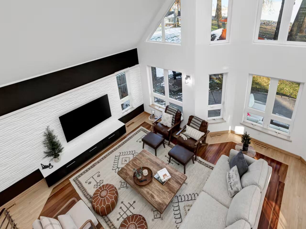 Ein modernes Wohnzimmer mit einem Flachbildfernseher, einem Holztisch, einer Couch und einem gemusterten Teppich.