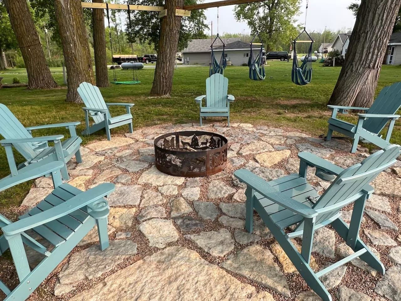A fire pit surrounded by Adirondack chairs in a stone-paved outdoor area.