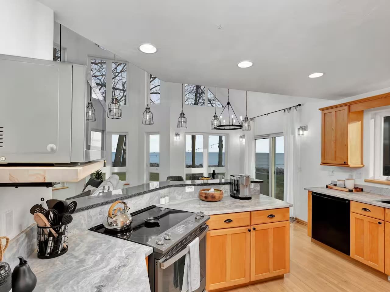 A modern kitchen with a large island, wooden cabinets, and pendant lighting.