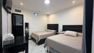 A hotel room with two beds, a desk with a telephone, and a flat-screen TV mounted on the wall.