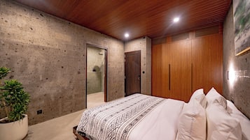 Un dormitorio con una cama, una planta en maceta, un armario de madera y una puerta.