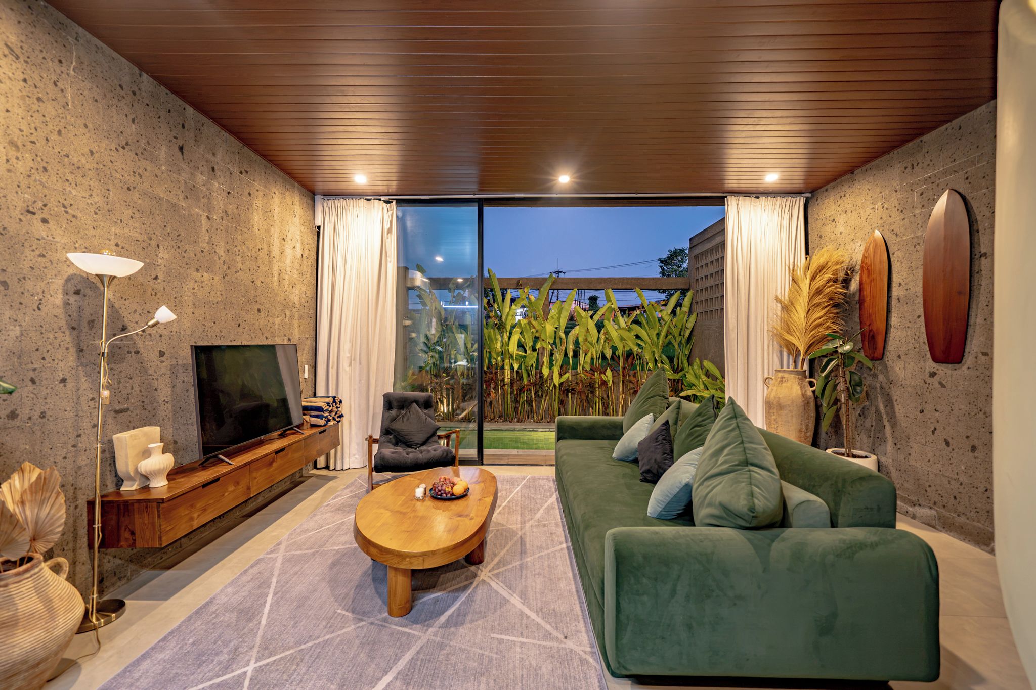 A modern living room with a green sofa, a wooden coffee table, and a TV on a wooden cabinet.