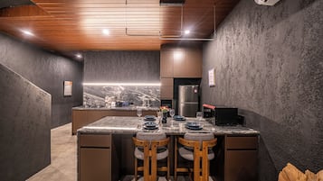 Una cocina moderna con encimera de mármol, taburetes de madera y refrigerador empotrado.