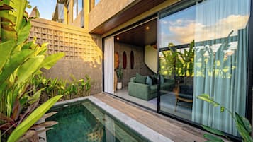 A modern outdoor pool area with a glass enclosure, a green sofa, and tropical plants.