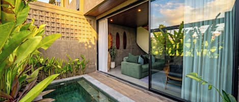 A modern outdoor pool area with a glass enclosure, a green sofa, and tropical plants.