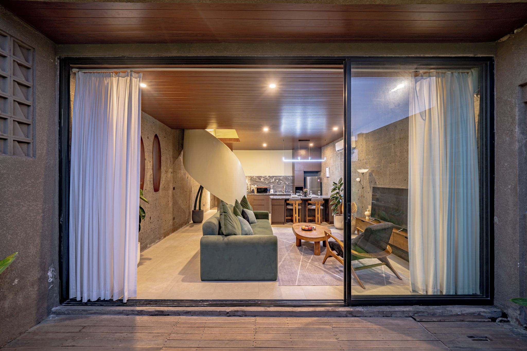 Un interior moderno con comedor, cocina y un amplio ventanal corredera que da a un espacio exterior.