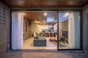 Un interior moderno con comedor, cocina y un amplio ventanal corredera que da a un espacio exterior.