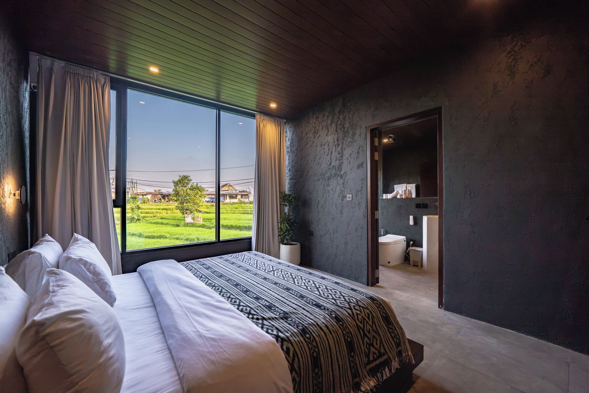 Un dormitorio con una cama grande, vistas a un campo verde y un baño visible a través de una puerta abierta.
