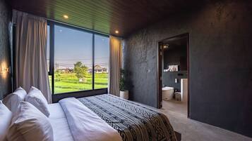 Un dormitorio con una cama grande, vistas a un campo verde y un baño visible a través de una puerta abierta.