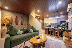 Un interior moderno con un sofá verde, una mesa de centro de madera, una zona de cocina y una escalera.