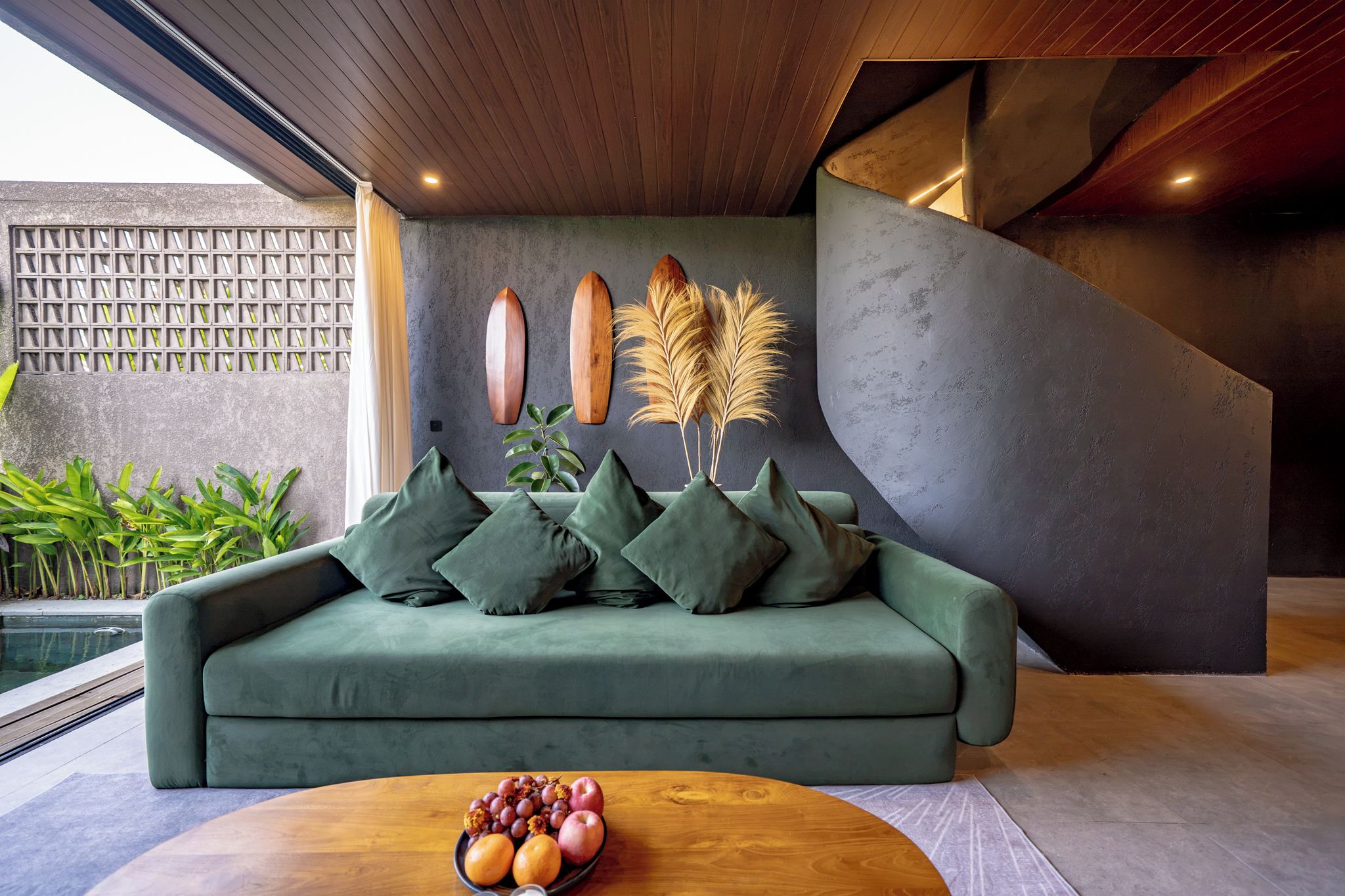 Una sala de estar moderna con un sofá verde, una mesa de centro de madera con fruta y objetos decorativos en la pared.