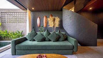 Una sala de estar moderna con un sofá verde, una mesa de centro de madera con fruta y objetos decorativos en la pared.
