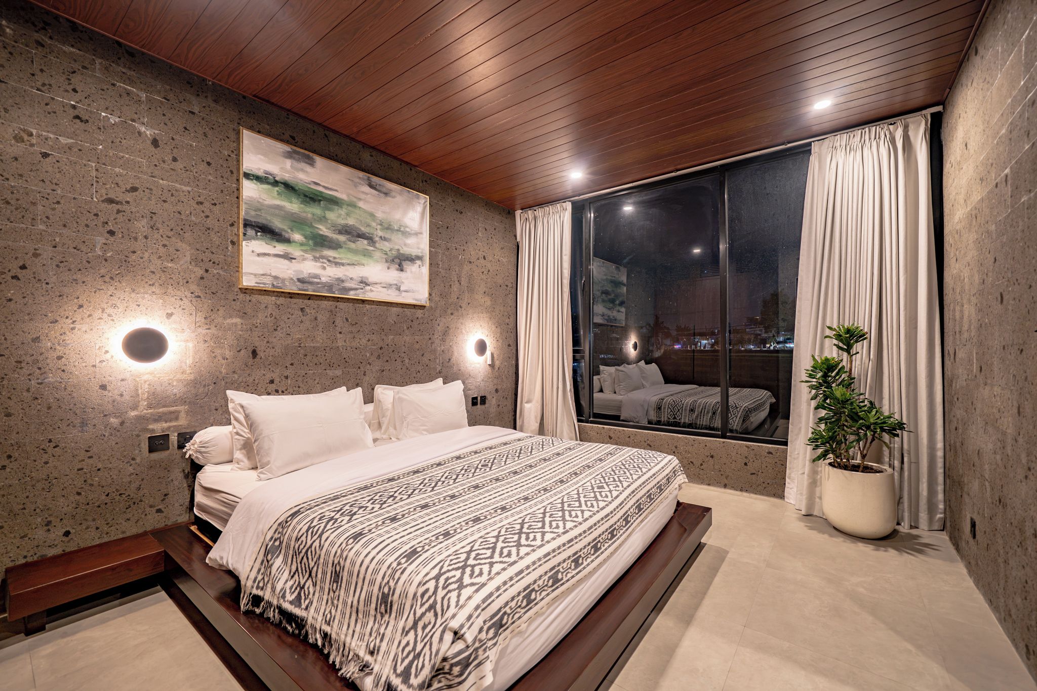 A modern bedroom with a large bed, a city view through a window, and a painting on the wall.