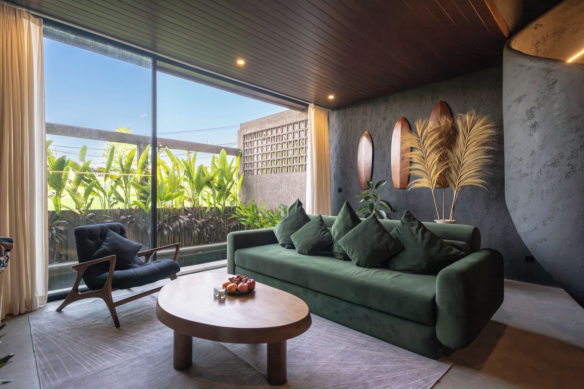 Una sala de estar moderna con un sofá verde, una mesa de centro redonda y vistas al exterior con vegetación.