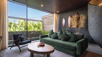 Una sala de estar moderna con un sofá verde, una mesa de centro redonda y vistas al exterior con vegetación.