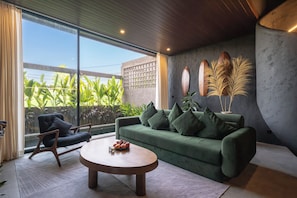 Una sala de estar moderna con un sofá verde, una mesa de centro redonda y vistas al exterior con vegetación.
