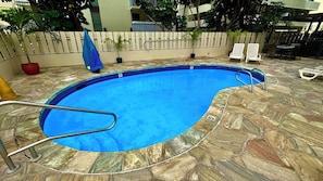A swimming pool with a stone surround, a metal ladder, and a fence. - Heart of Waikiki! 5 minutes to beach, Kitchenette, Two Beds, Sofa Bed (Honolulu)