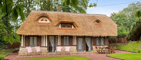 Una casa rústica con techo de paja, paredes de piedra y un pequeño porche con dos sillas.