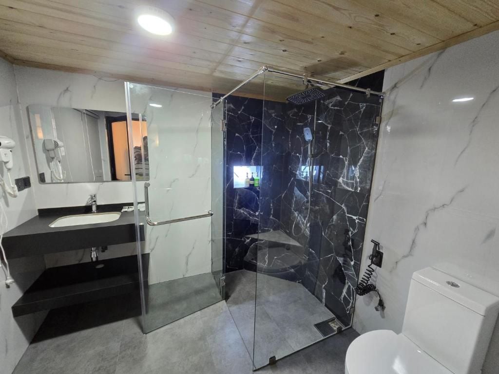 A modern bathroom with a glass-enclosed shower, a black countertop sink, and a white toilet.