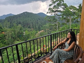 A person seated on a wooden bench with a view of a forested landscape and hills in the background. - Dewpoint Ella (Ella)