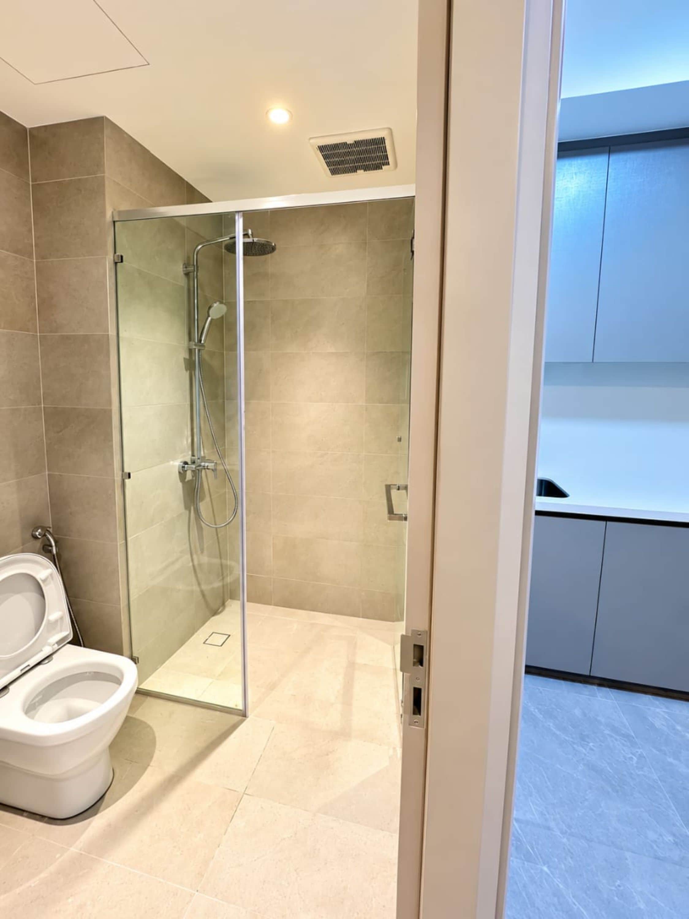 Un baño moderno con ducha de vidrio, inodoro y zona de lavamanos visible.