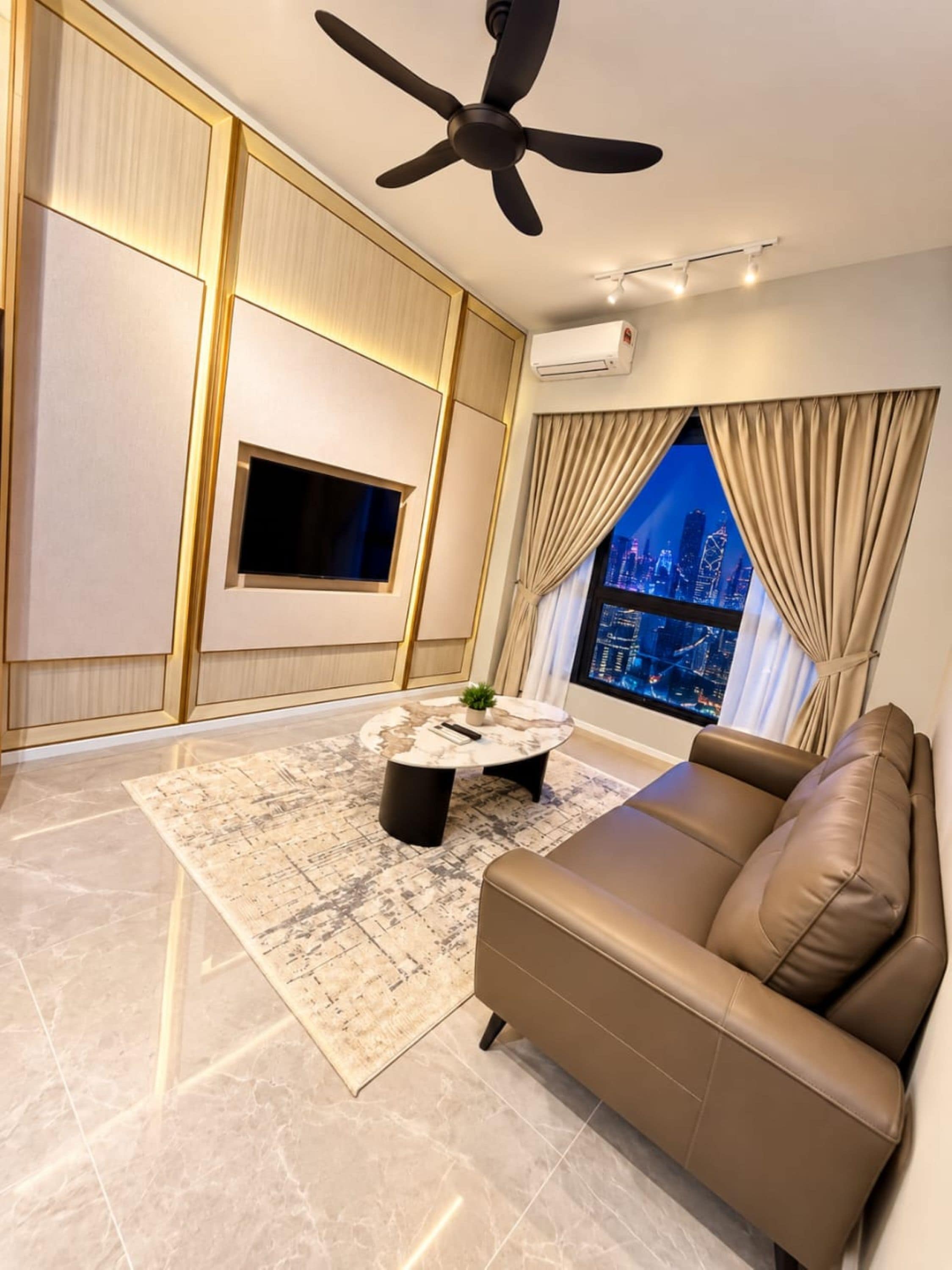 A modern living room with a ceiling fan, a flat-screen TV, a round coffee table, a sofa, and a large window with a city view.