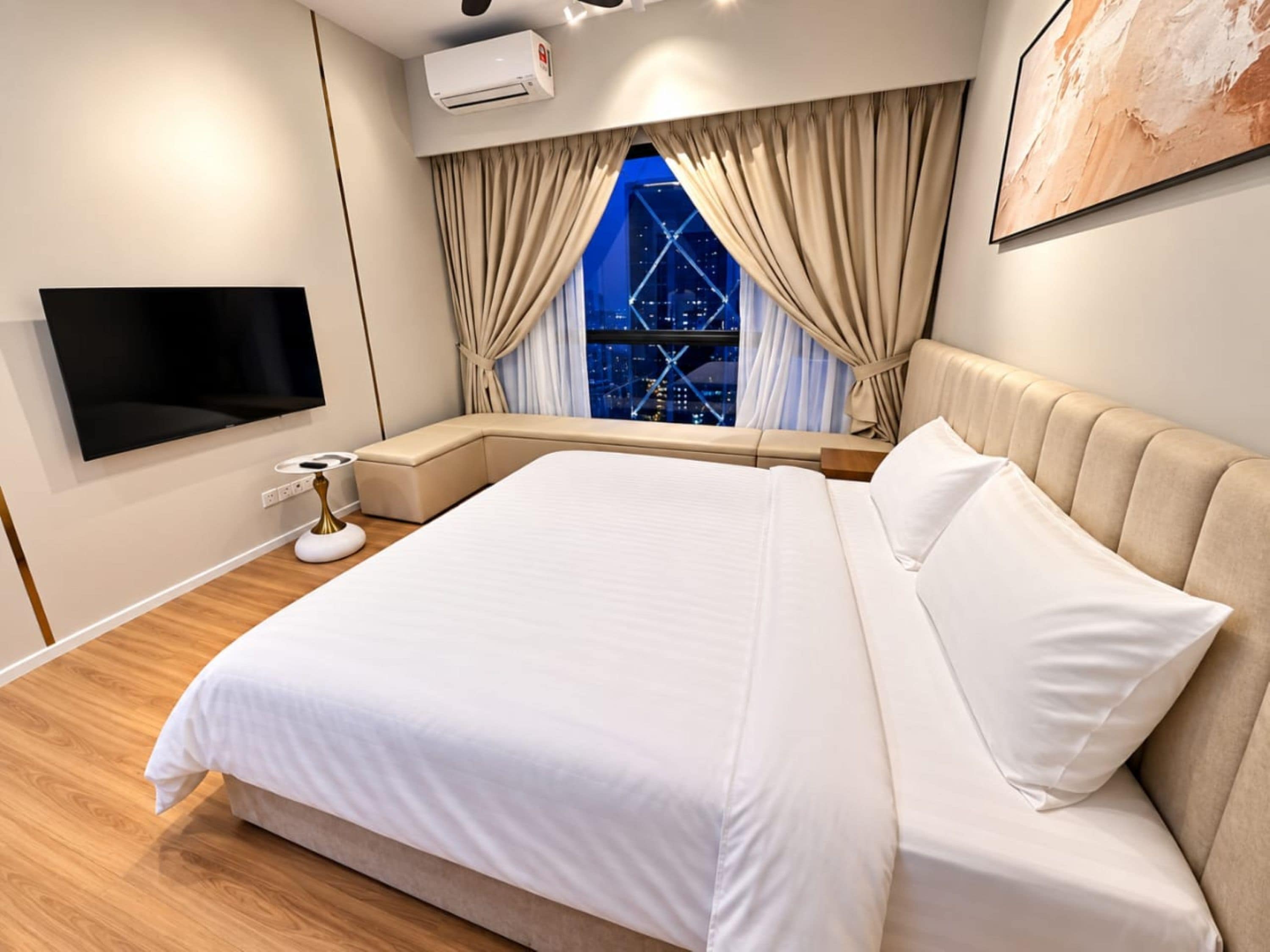 A modern bedroom with a large bed, a flat-screen TV, an air conditioning unit, and a window with curtains.
