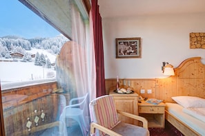 Ein Hotelzimmer mit einem hölzernen Bett, einem Nachttisch mit Lampe, einem Sessel und Blick auf schneebedeckte Berge.