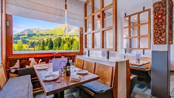 A restaurant with a large window offering a mountain view, wooden furniture, and a menu stand.