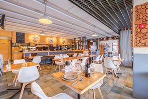 A restaurant interior with wooden tables, white chairs, hanging pendant lights, and a bar area with a menu board. - Hotel Relais Alpin Twin Room & Balcony 4 138 summer mode, Les Mosses, Switzerland (Les Mosses)