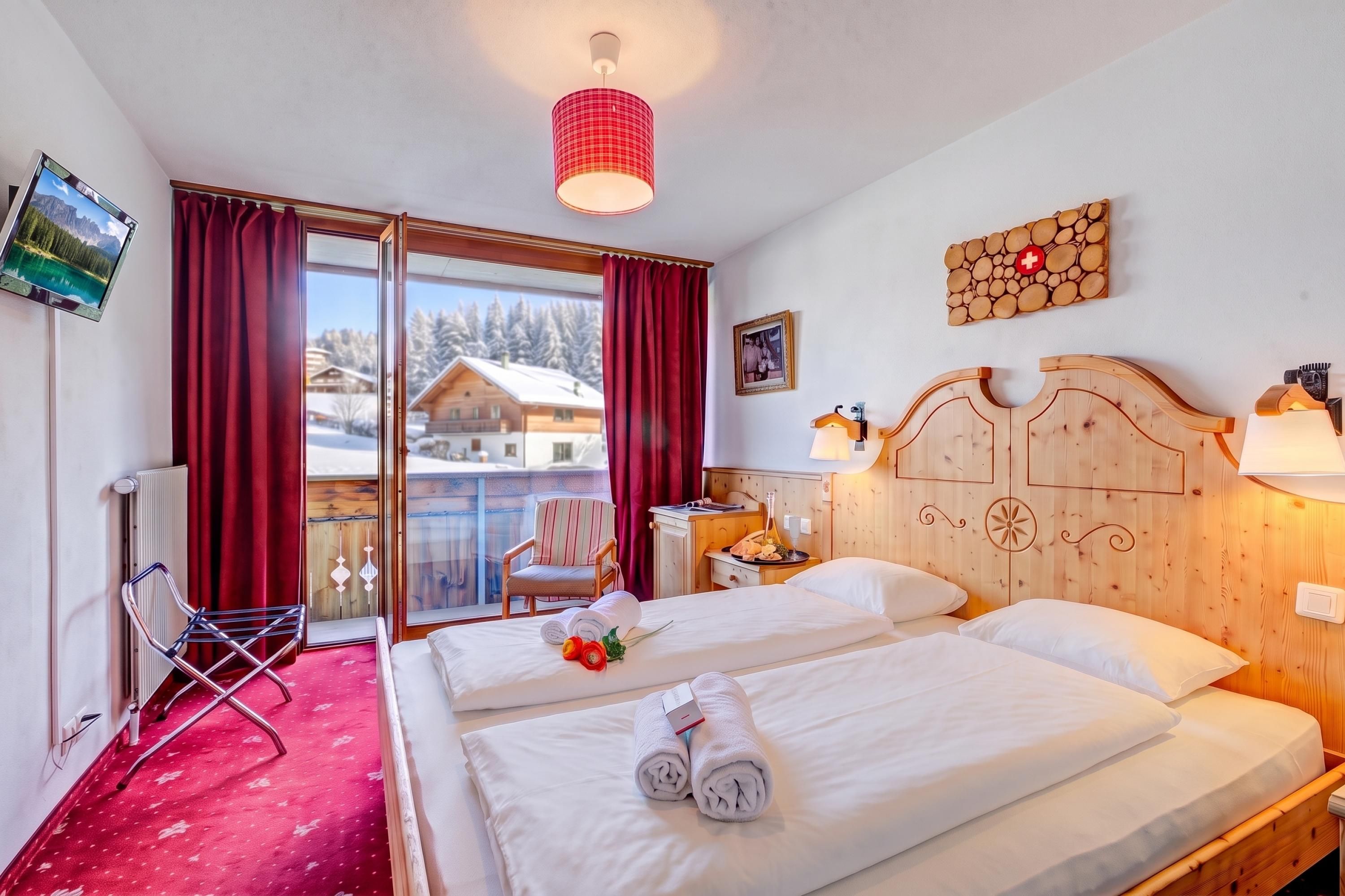 Une chambre d’hôtel avec un lit, une chaise, une télévision et une vue sur un chalet de montagne.
