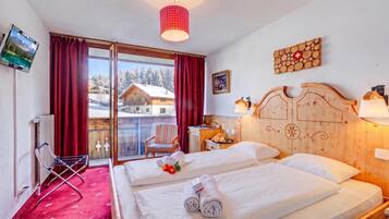 Une chambre d’hôtel avec un lit, une chaise, une télévision et une vue sur un chalet de montagne.