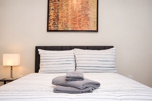 Een netjes opgemaakt bed met gestreept beddengoed, een kussen en een opgevouwen handdoek.