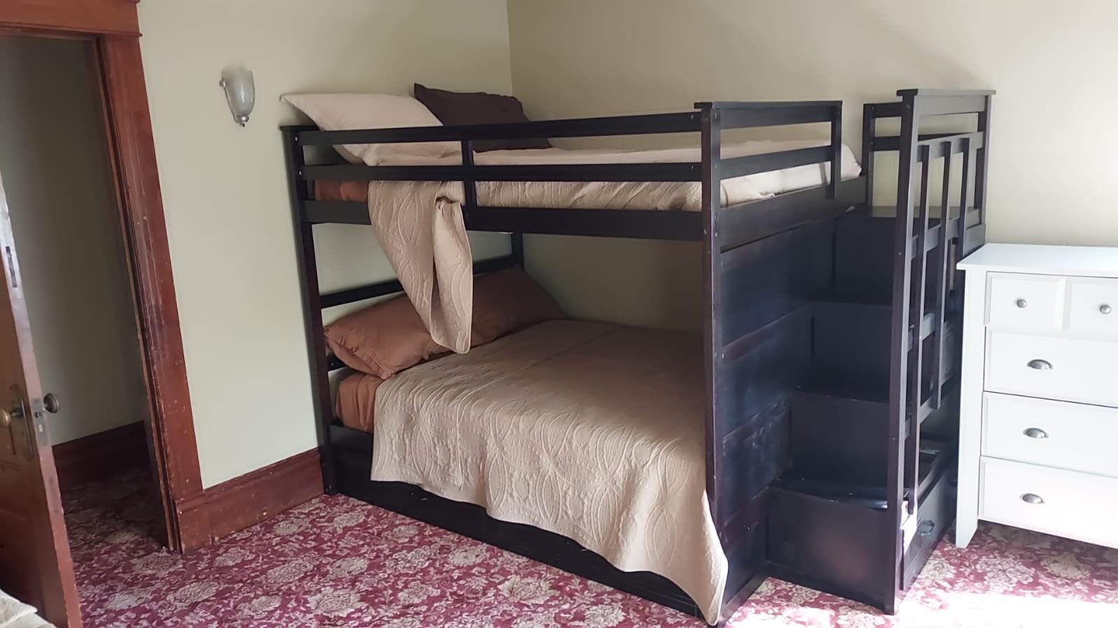 A bunk bed with a lower bunk, a white dresser, and a patterned carpet.