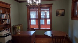 Una habitació amb escriptori de fusta, una cadira, una prestatgeria i una finestra amb cortines.