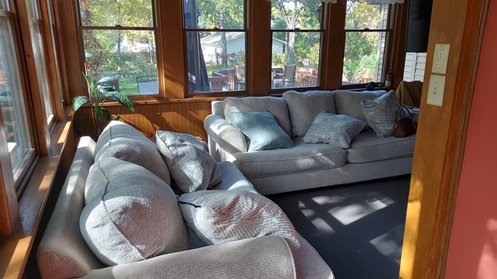 A sunlit room with a sectional sofa and a window overlooking a backyard.