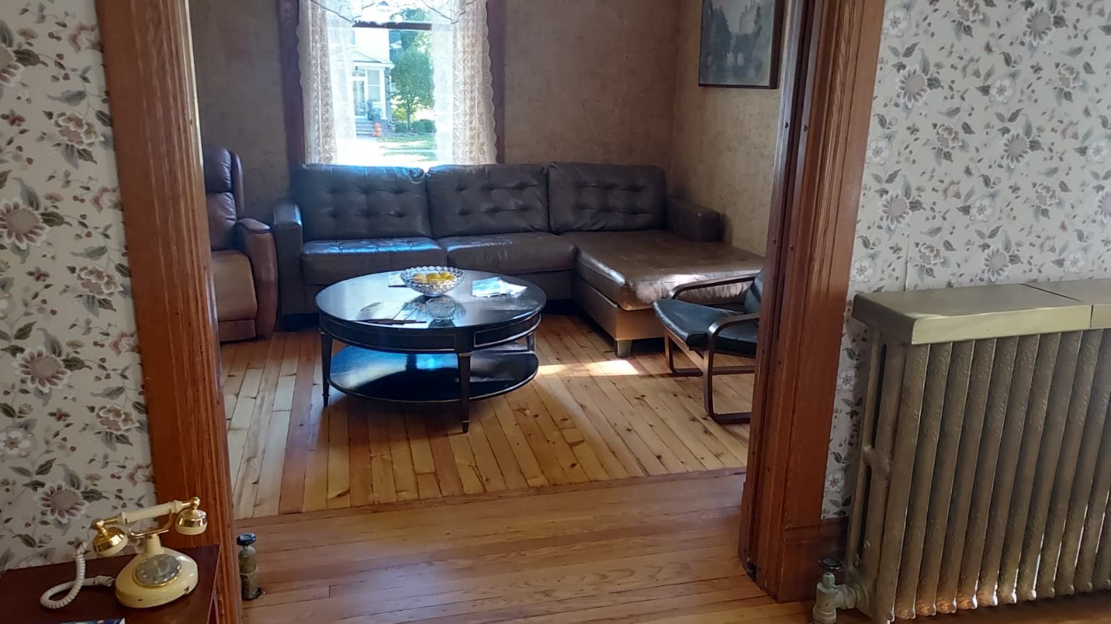 A room with a wooden floor, a round table with a bowl, a sofa, and a radiator.