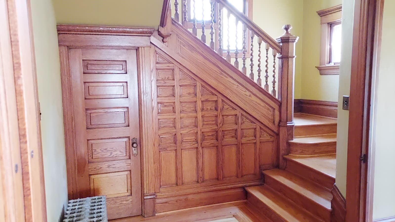 A wooden staircase with a handrail and a door with paneling.