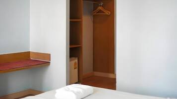 Una habitación de hotel con una cama, un armario de madera y un estante pequeño.
