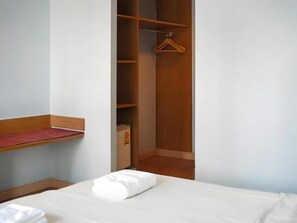 Una habitación de hotel con una cama, un armario de madera y un estante pequeño.