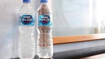 Dos botellas de agua Nestlé Pure Life sobre una superficie reflectante cerca de una ventana y una pared blanca con textura.