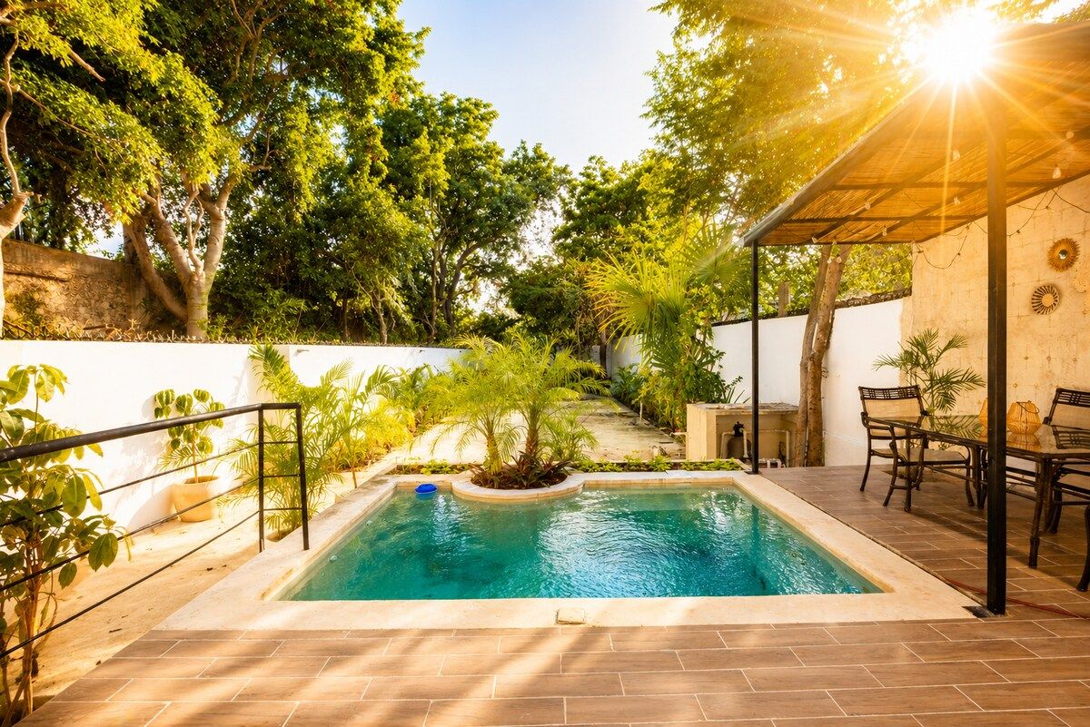 A swimming pool with a tiled deck, surrounded by greenery and a pergola.