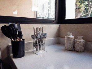 A kitchen counter with a utensil holder, two ceramic containers, and a window with a view of trees. - Casa Rita: Colonial Gem + Pool | Paseo Montejo (Merida)