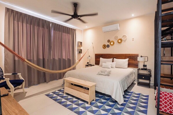 A bedroom with a bed, a hammock, a wooden bench, a nightstand, and a wall-mounted air conditioner. - Casa Rita: Colonial Gem + Pool | Paseo Montejo (Merida)
