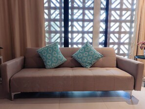 A beige sofa with two patterned cushions, positioned in front of a window with a lattice design. - Casa Rita: Colonial Gem + Pool | Paseo Montejo (Merida)