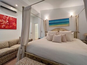 Un dormitorio con cama con dosel, dosel, un cuadro floral grande y un cuadro de una escena de playa.