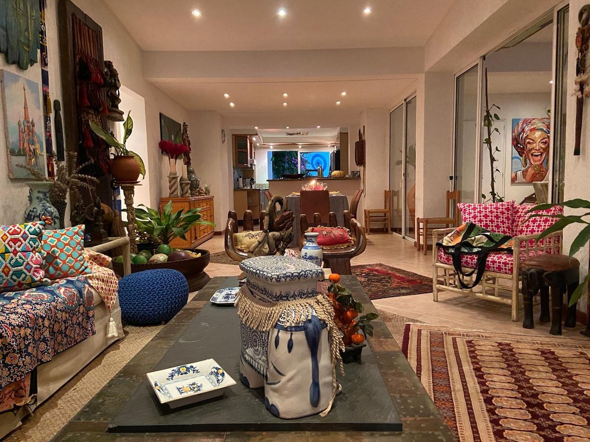 A spacious living room with a sofa, chairs, and a coffee table. There is a dining area in the background with a table and chairs.