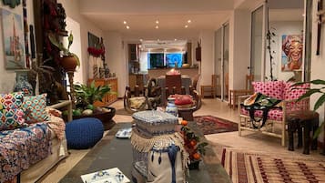 A spacious living room with a sofa, chairs, and a coffee table. There is a dining area in the background with a table and chairs.