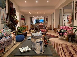 Un salón amplio con sofá, sillas y una mesa de centro. Se ve una zona de comedor al fondo, con una mesa y sillas.