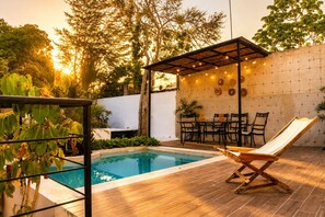 A swimming pool with a wooden deck, a lounge chair, and a covered seating area with string lights. - Casa  Alberca + Garaje | 2 cuadras Paseo Montejo (Merida)